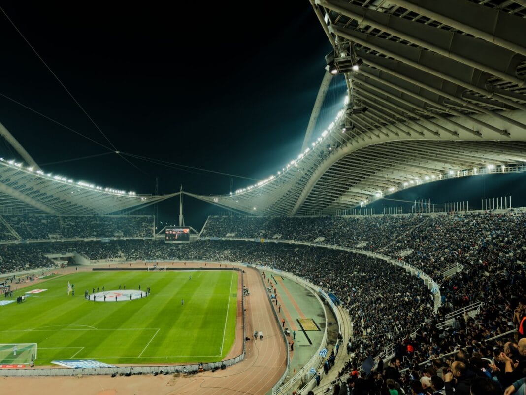 Zapełniony stadion piłkarski oświetlony nocą podczas meczu Zapełniony stadion piłkarski oświetlony nocą podczas meczu